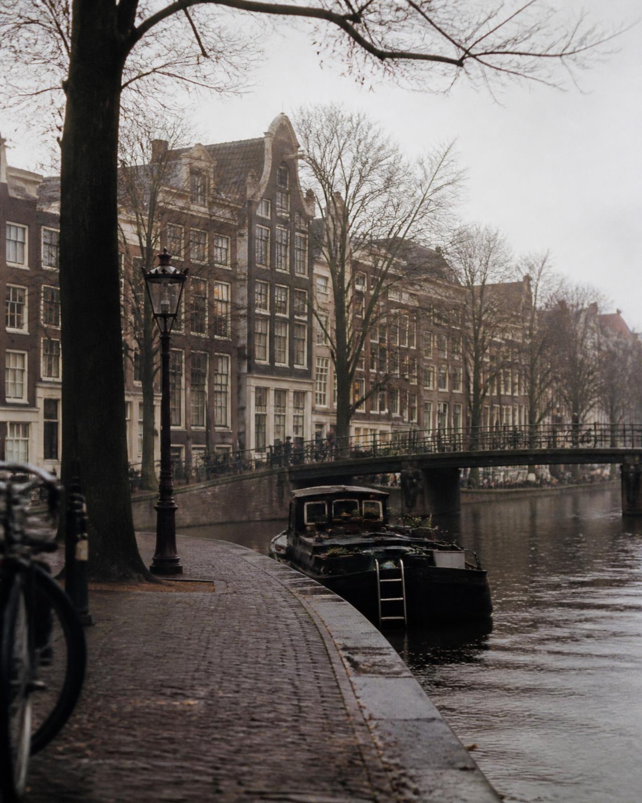 Dimmig morgon längs en kanal i Amsterdam med gavelhus som speglas i vattnet